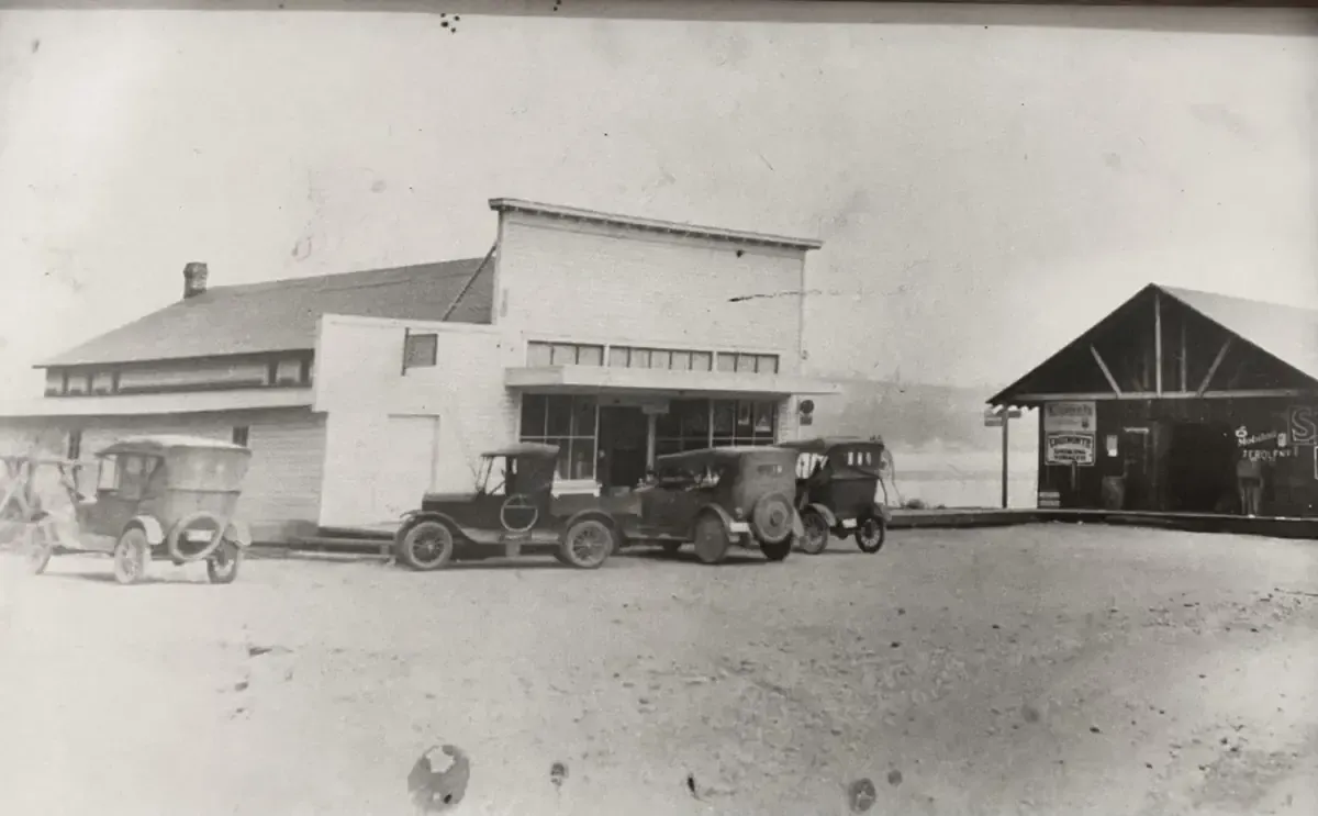 Black and white photo of the store with early automobiles parked out front and a Mobiloil sign on the shed next door