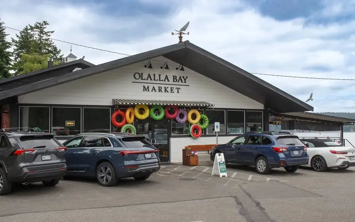 The Olalla Bay Market storefront by day, bright pool floats hung around the door and the bay behind
